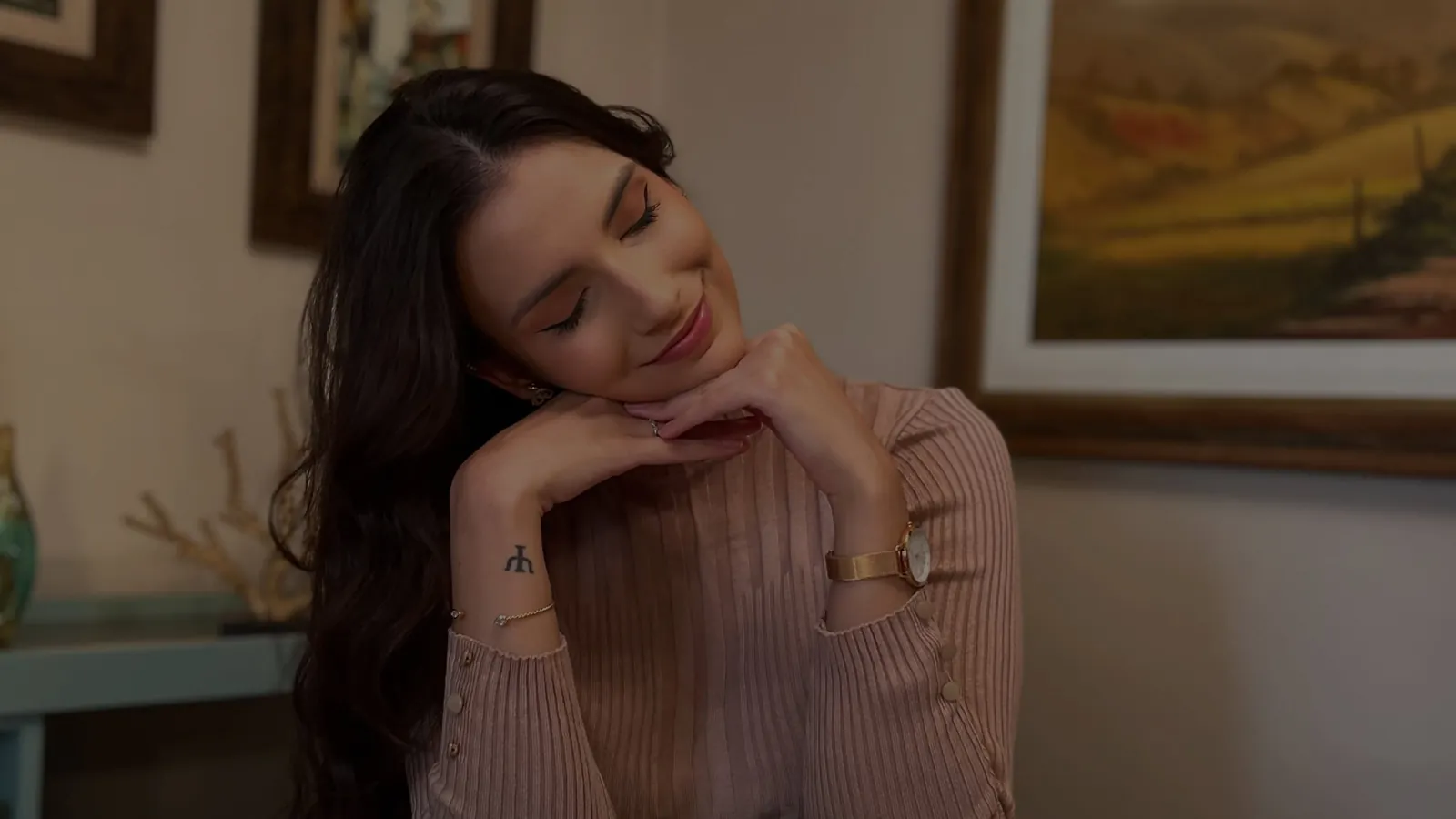 Juliana no consultório, de olhos fechados e sorrindo, com o rosto apoiado nas mãos
